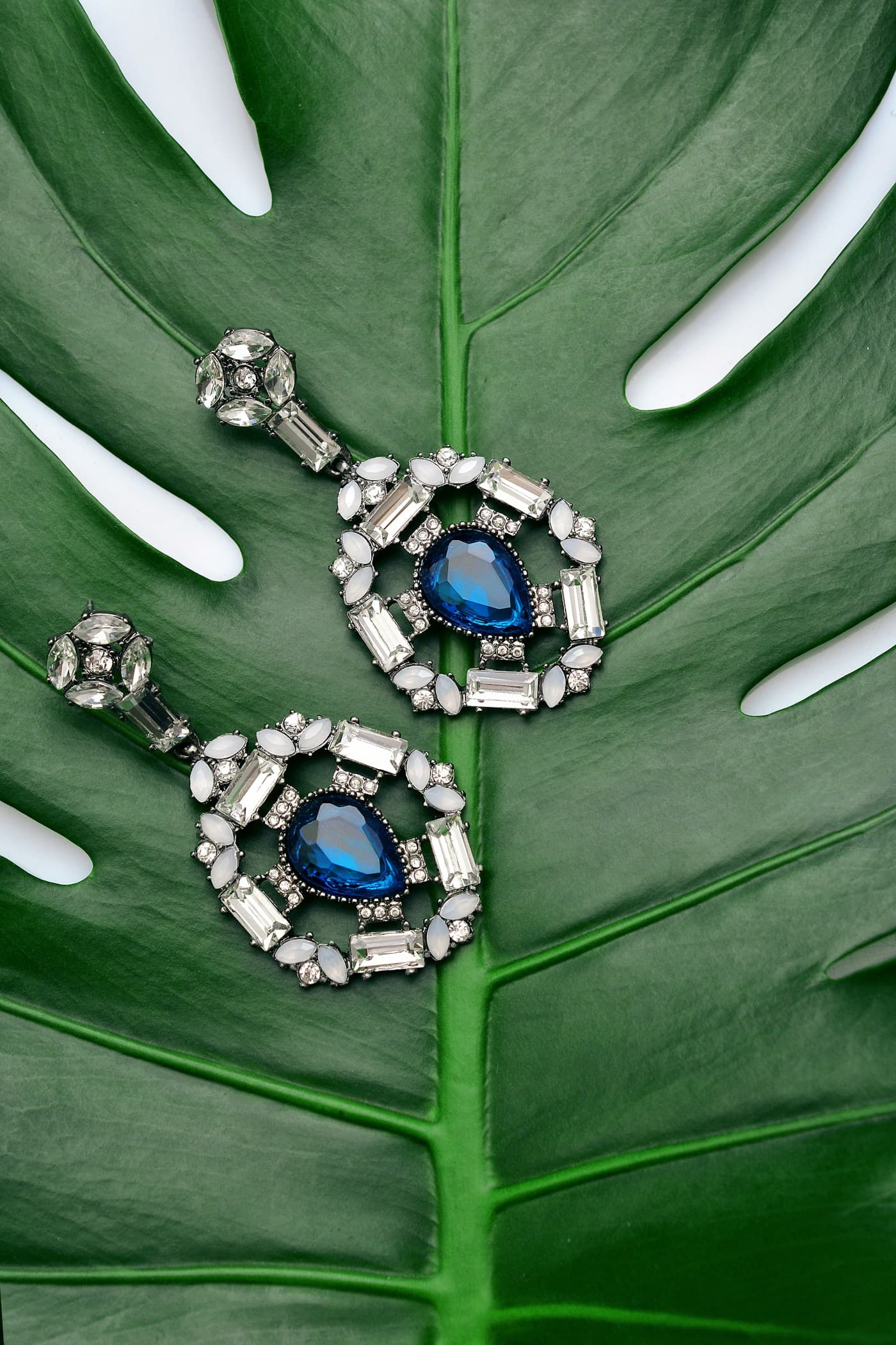 Blue stone drop earrings placed on a green leaf